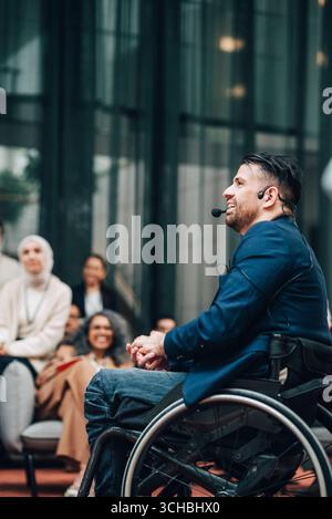 Un delegato di sesso maschile seduto su sedia a rotelle che tiene una lezione al seminario d'affari nel centro convegni Foto Stock