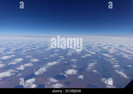 Nuvole soffici sparse di colore bianco con motivo che scompaiono verso l'orizzonte proiettano ombre sulla terra rossa dell'Australia centrale direttamente sotto, viste attraverso l'aereo wi Foto Stock