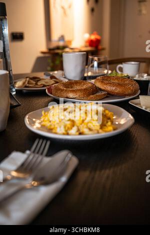 Un piatto di uova e pane tostato si siede su un tavolo in una stanza poco illuminata. Il tavolo è allestito con una varietà di piatti e utensili, tra cui forchetta, coltello e Foto Stock