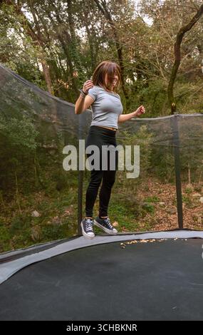 Una giovane donna vestita di abbigliamento sportivo è sospesa in aria dopo essere saltata su un trampolino all'aperto in montagna. Foto Stock