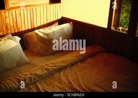 Luce del sole dorata mattutina su un intimo comodino in legno con cuscini a righe e una coperta Foto Stock