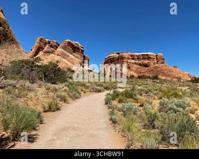Un sentiero che conduce attraverso la macchia e supera grandi formazioni rocciose sul Landscape Arch Trail nel Parco Nazionale di Arches, Moab, Utah, Stati Uniti Foto Stock