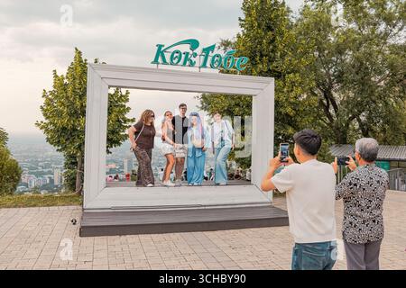 22 giugno 2025, Almaty, Kazakistan: Turisti che scattano foto di fronte a una cornice gigante nel parco Kok Tobe con la città sullo sfondo Foto Stock