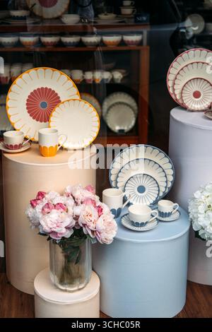 Set di stoviglie in ceramica colorata con motivi floreali grafici esposti su piedistalli pastello accanto alle peonie fresche. Estetica domestica, vita lenta Foto Stock