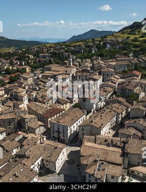 Veduta aerea dei tetti di terracotta che scendono lungo la collina, incorniciati da montagne verdeggianti e dal lontano cielo blu, Pescocostanzo, Abruzzo, Italia. Foto Stock
