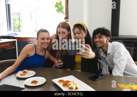 Diversi adolescenti che scattano selfie insieme a casa, gustando spuntini e festeggiando l'amicizia. celebrazione, divertimento, felicità, gioventù, riunione, incollaggio Foto Stock