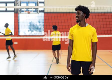 Diversi compagni di squadra maschili in maglie gialle giocano a pallavolo sul campo vicino alla rete, copia spazio. Atletismo, lavoro di squadra, competizione, intensità, fitness, rec Foto Stock