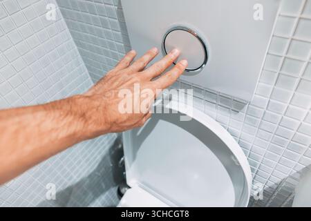 Premendo a mano un pulsante a filo su un WC moderno, sfoggia un design elegante in un bagno pulito e piastrellato con dettagli eleganti Foto Stock