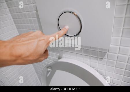 Premendo a mano un pulsante a filo su un WC moderno, sfoggia un design elegante in un bagno pulito e piastrellato con dettagli eleganti Foto Stock