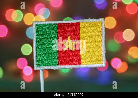 Bandiera camerunese ricamata di fronte ai fuochi d'artificio bokeh arcobaleno, che rappresentano il Capodanno o le festività nazionali con un'atmosfera festosa. Foto Stock