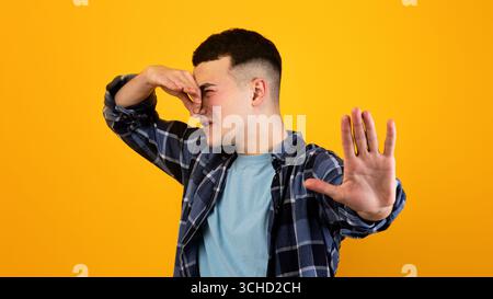 Giovane caucasico che chiude il naso, soffrendo di cattivo odore, gesturing STOP su sfondo arancione studio Foto Stock
