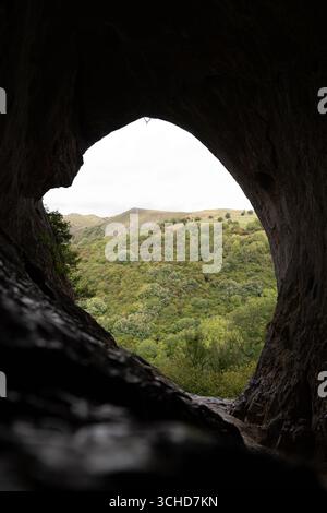 Vista dall'interno della Thor's Cave che incornicia una valle verde nel Peak District National Park, Regno Unito, in una giornata nuvolosa Foto Stock
