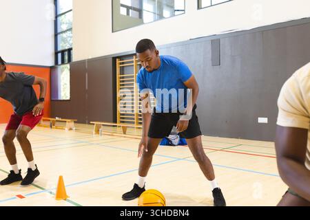 Compagni di squadra di basket afroamericani che praticano palle di palle da palle di palle di palle di pallacanestro intorno ai coni in palestra Foto Stock