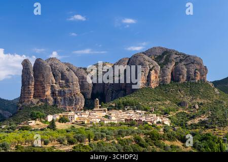 Pittoresco paesaggio che mostra il villaggio di Aguero con le sue case tradizionali sotto le torreggianti formazioni rocciose di Mallos de Aguero, una meraviglia geologica Foto Stock