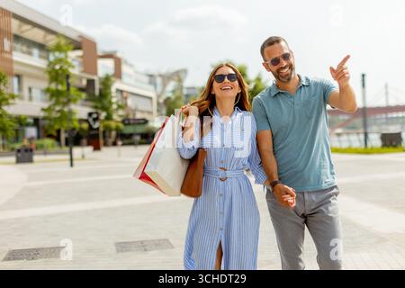 Il sole riempie l'aria mentre una coppia felice cammina mano nella mano, chiacchiera e ridendo. Le loro borse per lo shopping suggeriscono una deliziosa giornata trascorsa alla scoperta del Foto Stock