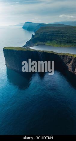 Le maestose scogliere sorgono drammaticamente dalle tranquille acque delle Isole Faroe, bagnate dalla luce soffusa del sole. Lago Sorvagsvatn Foto Stock