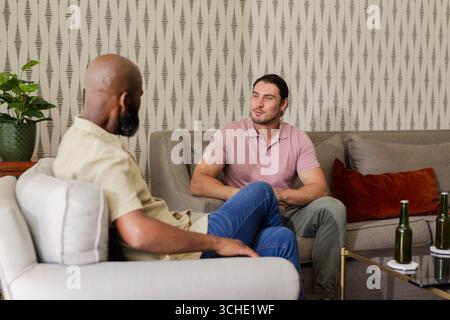 Chiacchierando con diversi amici maschi seduti in un moderno soggiorno, con tavolino da caffè e bottiglie verdi Foto Stock