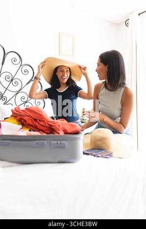 Diverse amiche che portano la valigia a casa, provano i cappelli e ridono insieme Foto Stock