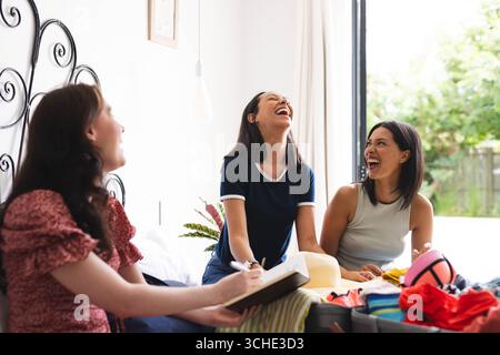 Diverse amiche che ridono insieme mentre preparano la valigia per le vacanze a casa Foto Stock