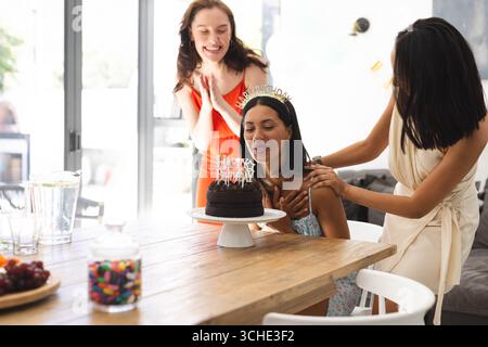 Festeggiamo il compleanno, le diverse e gioiose amiche femminili sorprendono la donna con la torta a casa Foto Stock