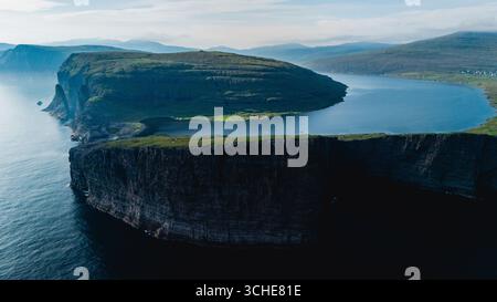 Un'impressionante prospettiva aerea rivela le aspre scogliere e le tranquille acque delle Isole Faroe. Il lussureggiante paesaggio verde contrasta con il mare blu profondo, creando un'atmosfera serena. Foto Stock