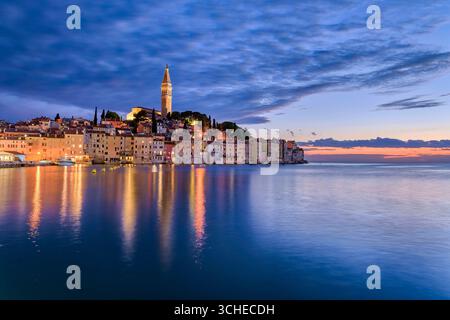 Case nella città costiera di Rovigno e il campanile della chiesa di Sant'Eufemia, viste sopra le acque del Mar Mediterraneo al tramonto. Rovigno IST Foto Stock