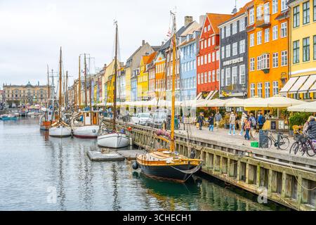 I visitatori esplorano la vivace zona di Nyhavn a Copenaghen, Danimarca, dove le storiche barche in legno fiancheggiano il canale sullo sfondo di edifici colorati e vivaci caffetterie. Foto Stock
