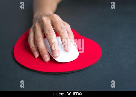 Mano della donna che fa clic sul mouse, poggia il polso sul tappetino rosso per poggiapolso. Primo piano. Foto Stock