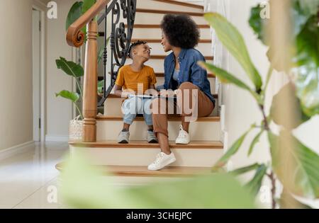 Madre e figlio seduti sulle scale, a leggere libri e a condividere momenti di gioia Foto Stock