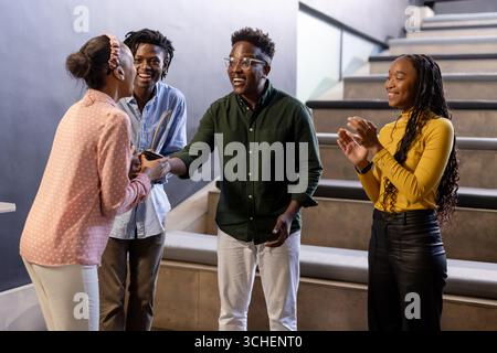 Colleghi eterogenei che celebrano il successo, stringono la mano e battono le scale moderne dell'ufficio Foto Stock
