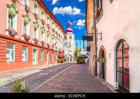 Strada colorata nel centro storico di Ptuj, Slovenia, con vista sull'iconica torre della chiesa. Foto Stock