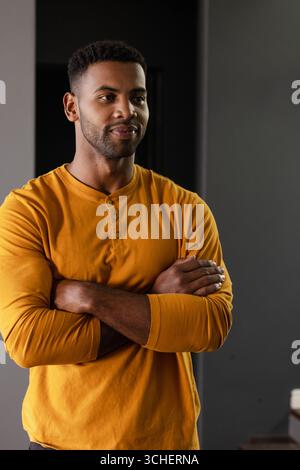 Uomo sicuro di sé con la camicia di senape in piedi con le braccia incrociate, sorridendo calorosamente Foto Stock