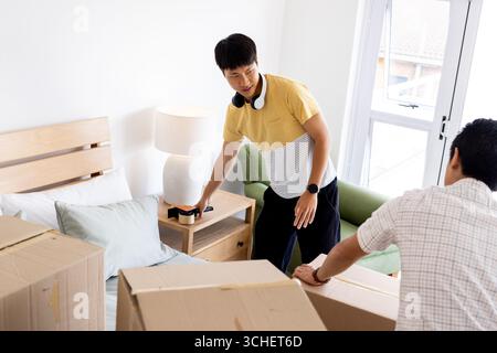 Giovane che disimballa scatole in camera da letto, organizzando una nuova casa con la famiglia Foto Stock