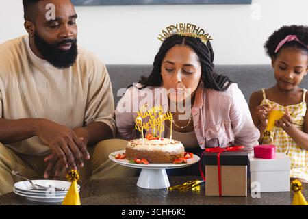 Festeggia il compleanno, donna che soffia candele sulla torta con la famiglia felice a casa Foto Stock