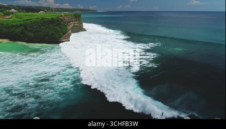 Splendida vista aerea delle grandi onde che si snodano verso la riva di Dreamland Beach in una splendida giornata di sole, Bali, Indonesia, con i surfisti che si godono le potenti onde Foto Stock