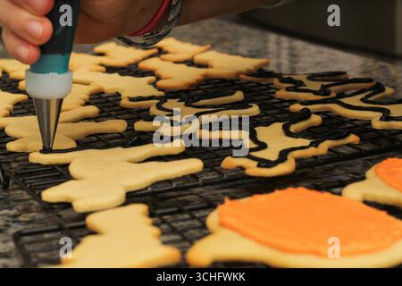 Versare la glassa nera sui biscotti di Halloween Cat Foto Stock