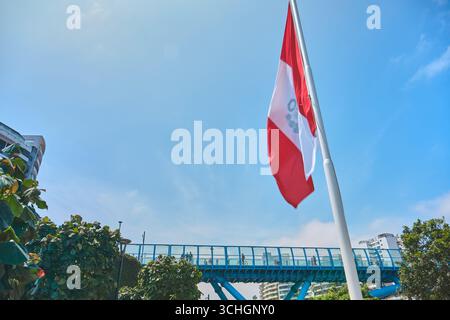 Lima perù agosto 30 2025: Bandiera peruviana rossa e bianca sventolando nel vento con il nuovo ponte la paz sullo sfondo Foto Stock
