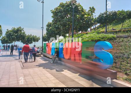Lima perù agosto 30 2025: Persone che si godono una giornata di sole a miraflores, lima, perù, camminando vicino al colorato cartello di miraflores con il nuovo ponte visibile nel backgroun Foto Stock