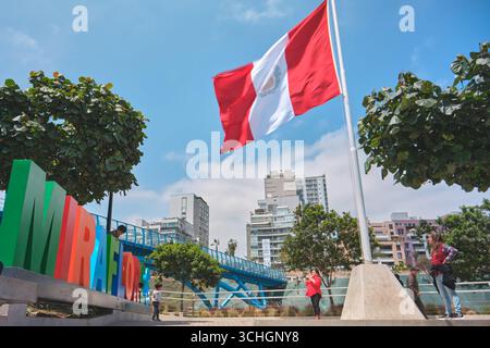Lima perù agosto 30 2025: Grande bandiera peruviana che sventola orgogliosamente in un parco di miraflores, con il nuovo ponte la paz sullo sfondo Foto Stock