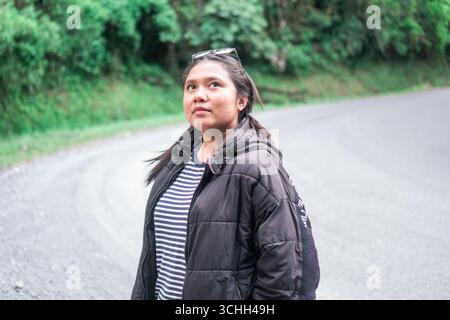 Donna asiatica che indossa una giacca calda e una camicia a righe in piedi sulla strada di montagna Foto Stock