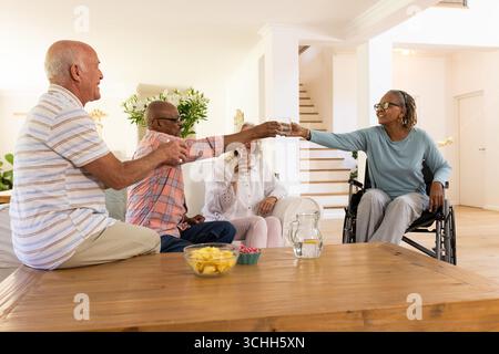Amici anziani che brindano con bevande a casa, godendosi una conversazione allegra insieme Foto Stock