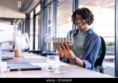 Uomo sorridente che usa un tablet alla scrivania dell'ufficio, si impegna in un lavoro creativo, si copia spazio Foto Stock