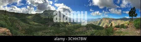 Ampio panorama caratterizzato da una vivace valle verde, montagne lontane e un cielo luminoso e soleggiato. Foto Stock