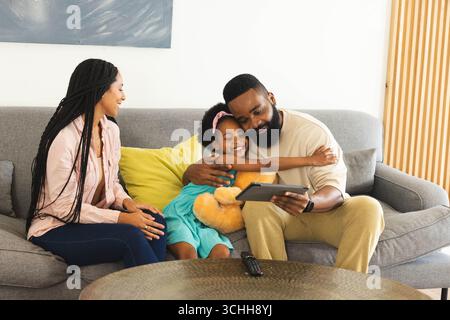 Famiglia felice che si diverte a trascorrere momenti di qualità sul divano, padre che tiene il tablet, figlia che lo abbraccia, a casa Foto Stock