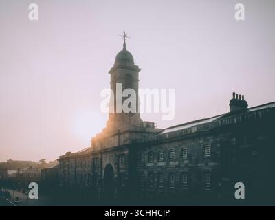 Alba dietro la torre dell'orologio in una mattina nebbiosa al Royal William Yard di Plymouth, Devon Foto Stock