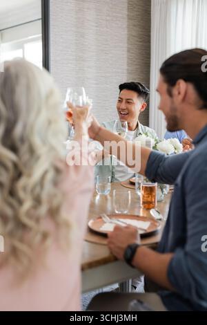 Gli amici brindano con un drink al ricevimento di nozze, festeggiando con gioia e risate Foto Stock
