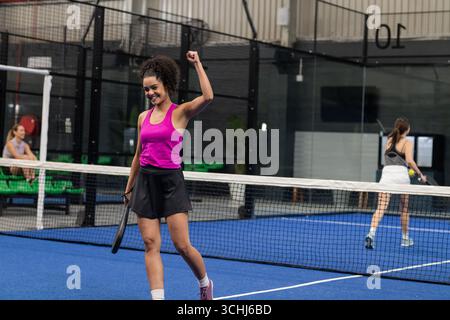 Donna ispanica o latina che puzza e sorride sul campo blu del padel con racchetta, rete Foto Stock