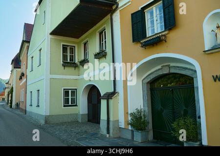 Foto di una strada acciottolata a Wachau, Austria. La prima casa è gialla con cancelli verdi e vasi di fiori, seguita da affascinanti case arancioni lungo il Foto Stock
