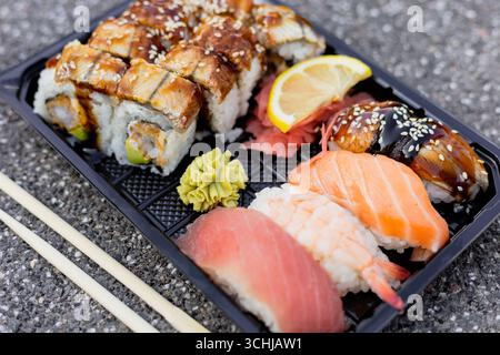 Una vasta selezione di sushi è disposta su un vassoio nero, con panini ricoperti di anguille e fette di limone, oltre a vivaci nigiri e wasabi Foto Stock