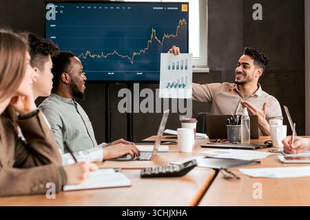 Dipendente che mostra carta con diagramma grafico, seduto alla scrivania Foto Stock